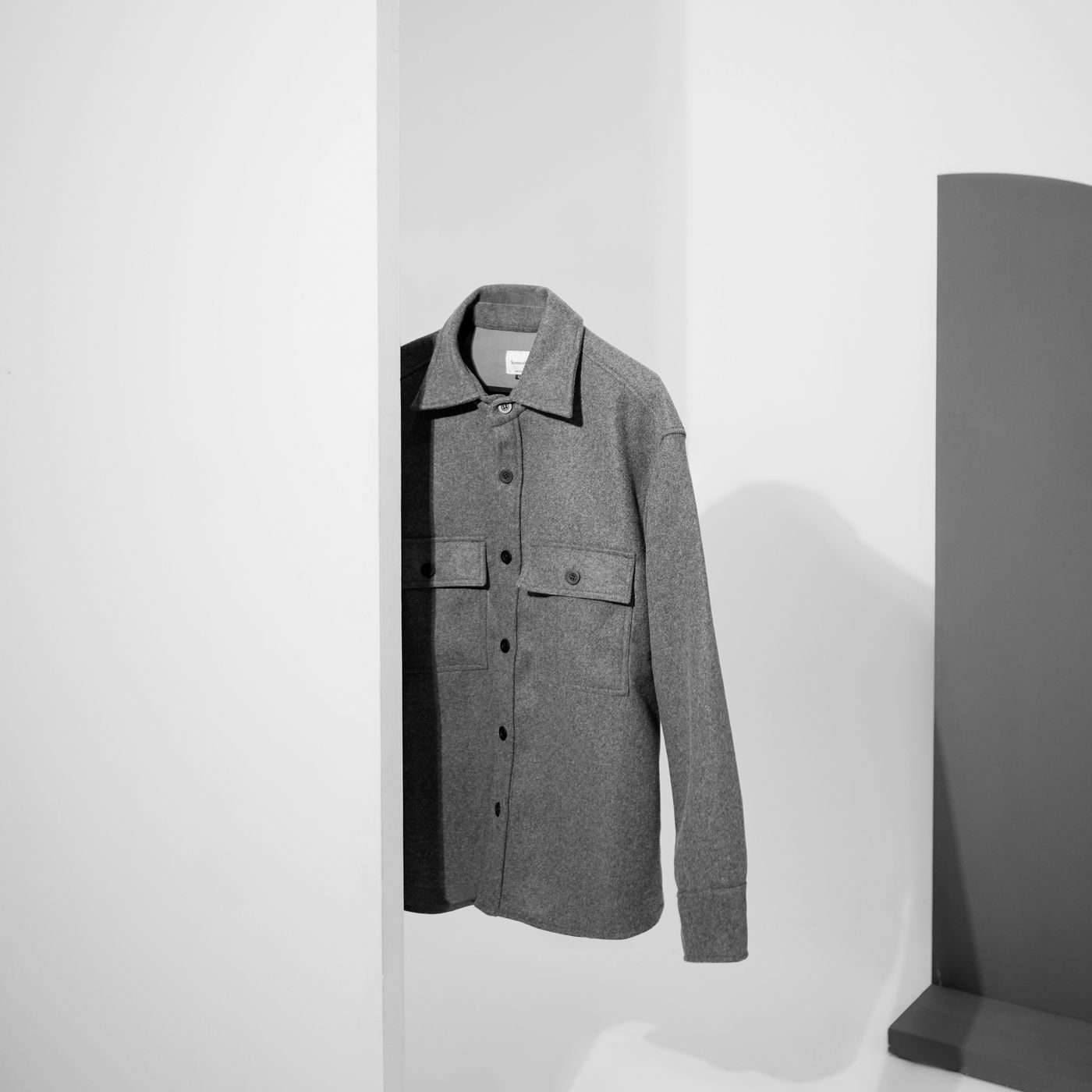 Monoloom Warp Overshirt, a grey wool overshirt hung against a white wall