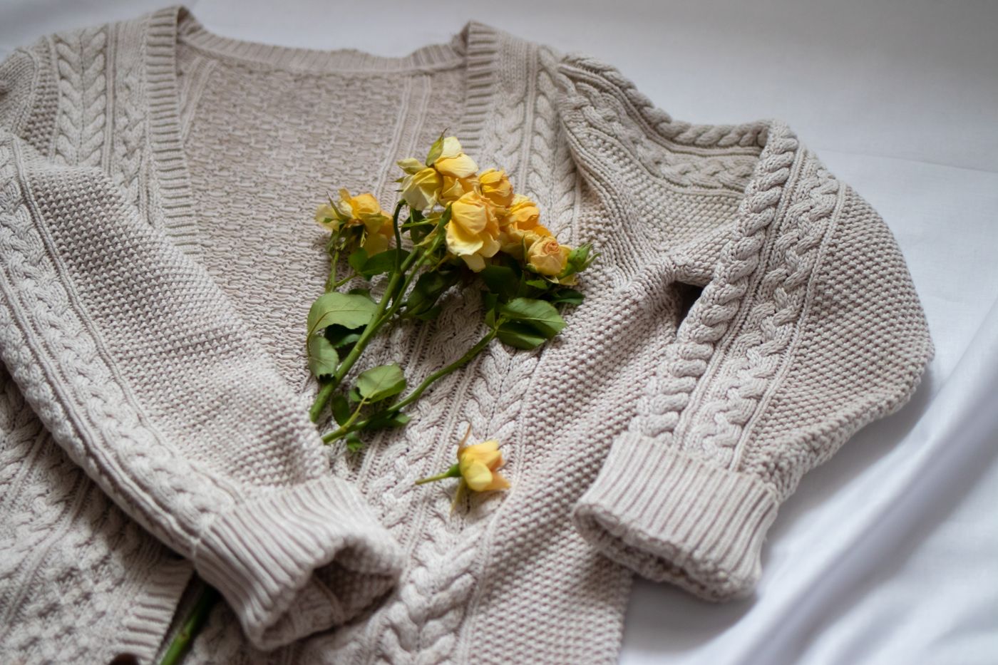 Monoloom Ground Cardigan, a cream cable cardigan laid flat